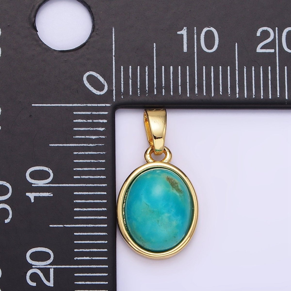 Gold pendant with a turquoise stone on a ruler for scale