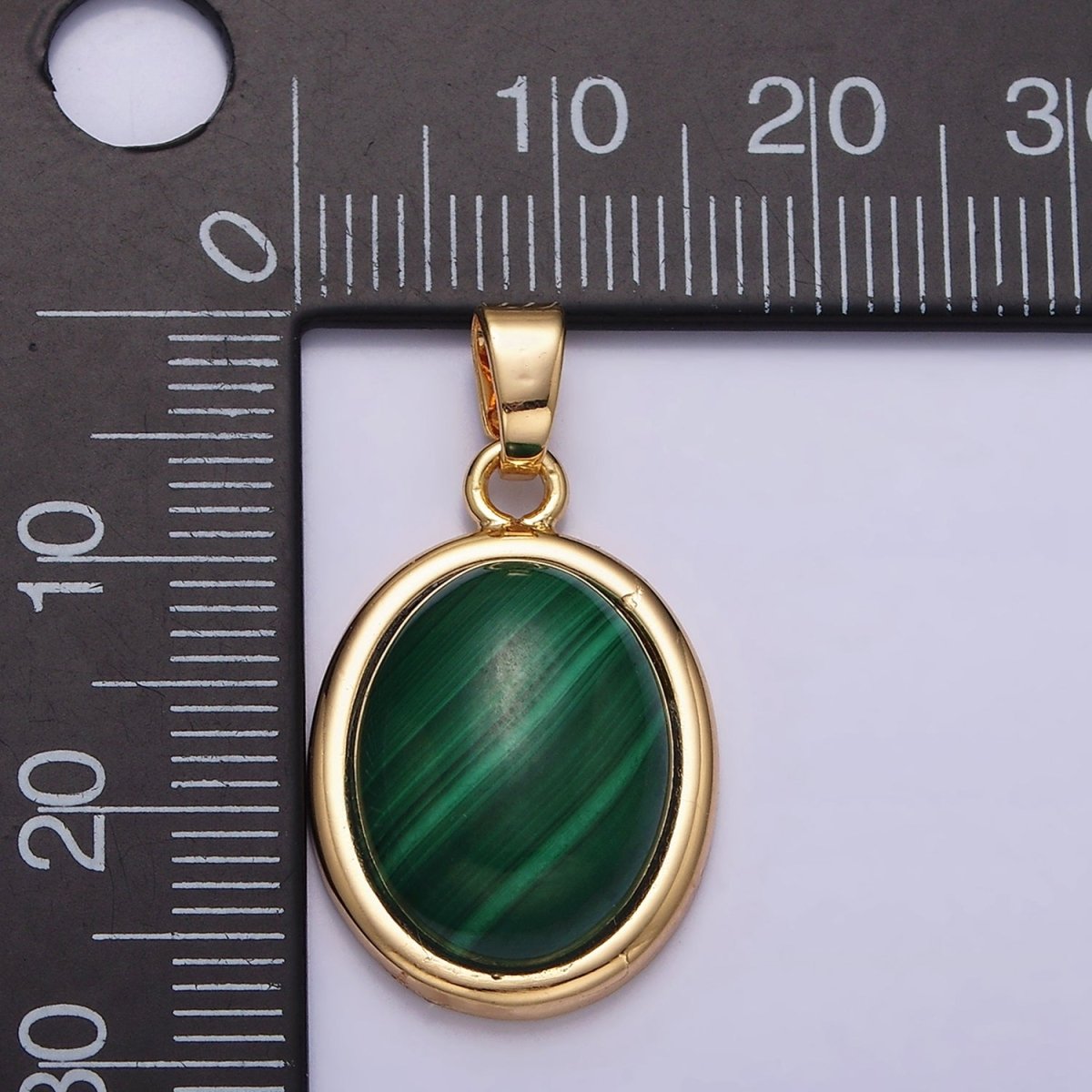 Gold pendant with green stone on a ruler for scale