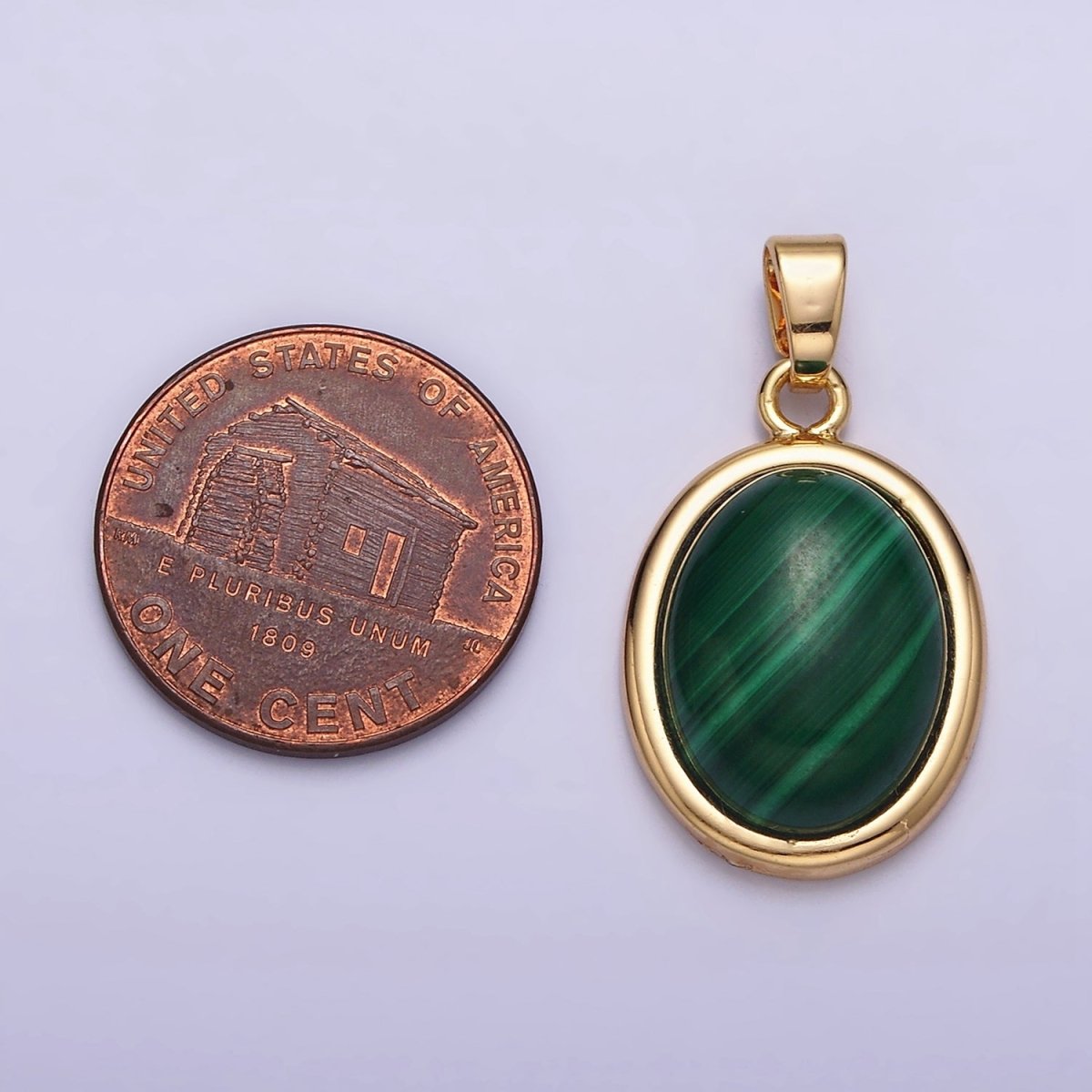 Gold pendant with green stone next to a penny on a light purple background