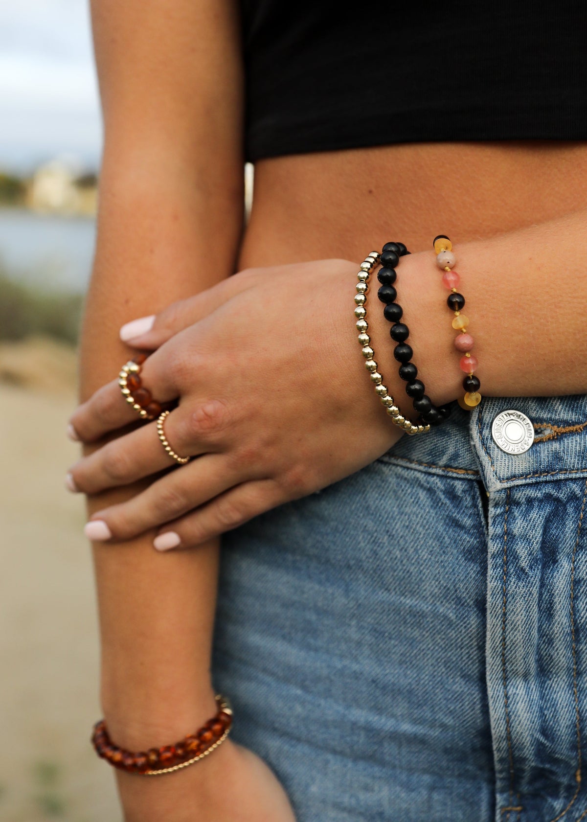 Close-up of a person's arm with multiple bracelets and rings, wearing a black top and blue jeans.