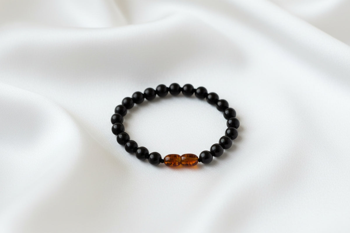 Black beaded bracelet with a single amber bead on a white background