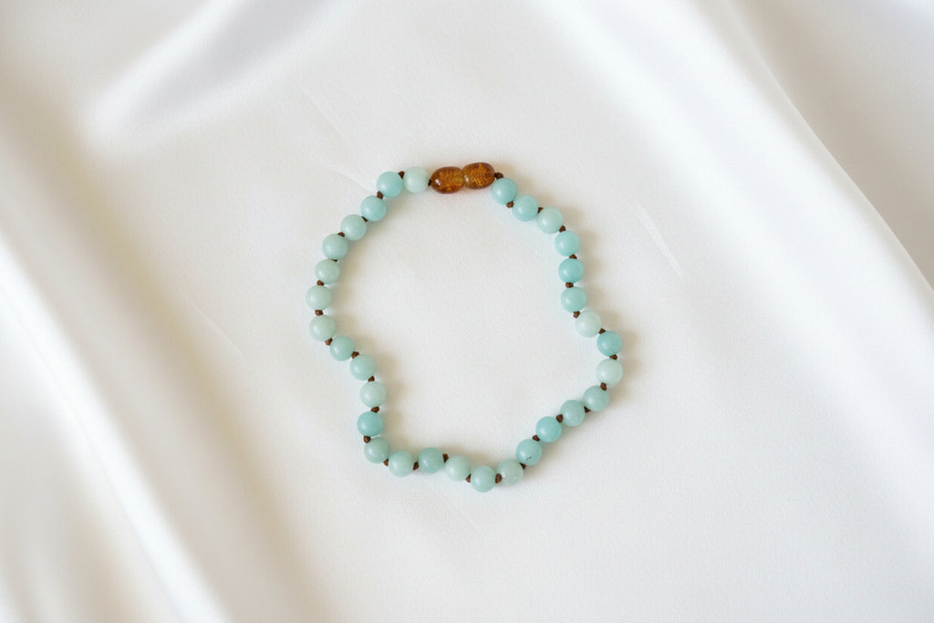 A beaded necklace with light blue-green round beads and a small brown polished accent bead at the top, photographed on a plain white background.