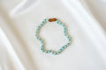 A beaded necklace with light blue-green round beads and a small brown polished accent bead at the top, photographed on a plain white background.