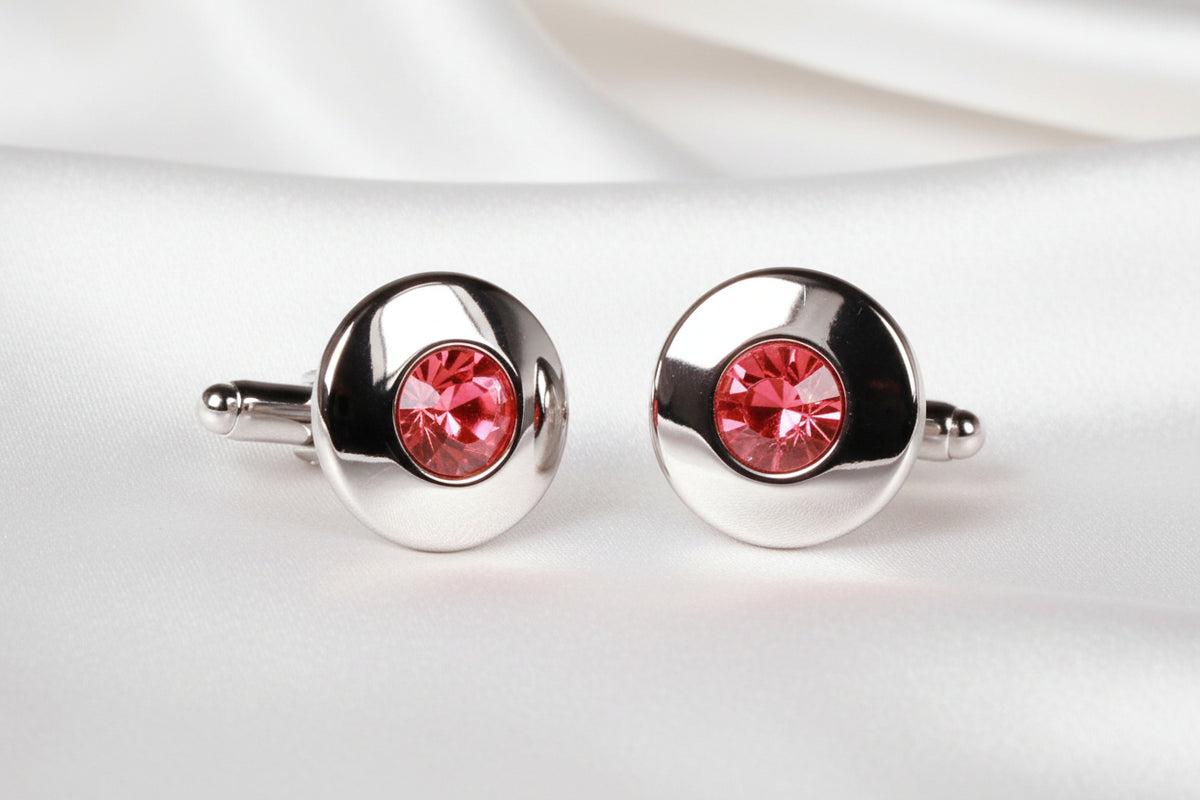 A pair of silver-toned oval cufflinks, each featuring a round faceted pink gemstone in the center, shown against a plain white background.
