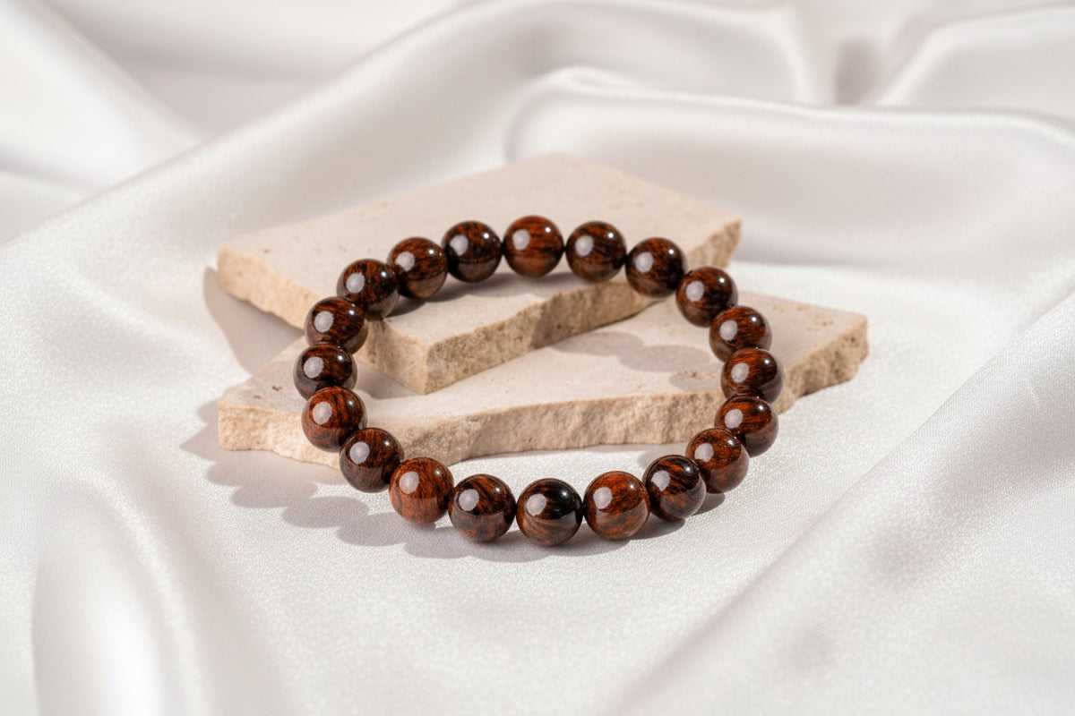 A beaded stretch bracelet made of glossy dark brown and black round beads, silky white background