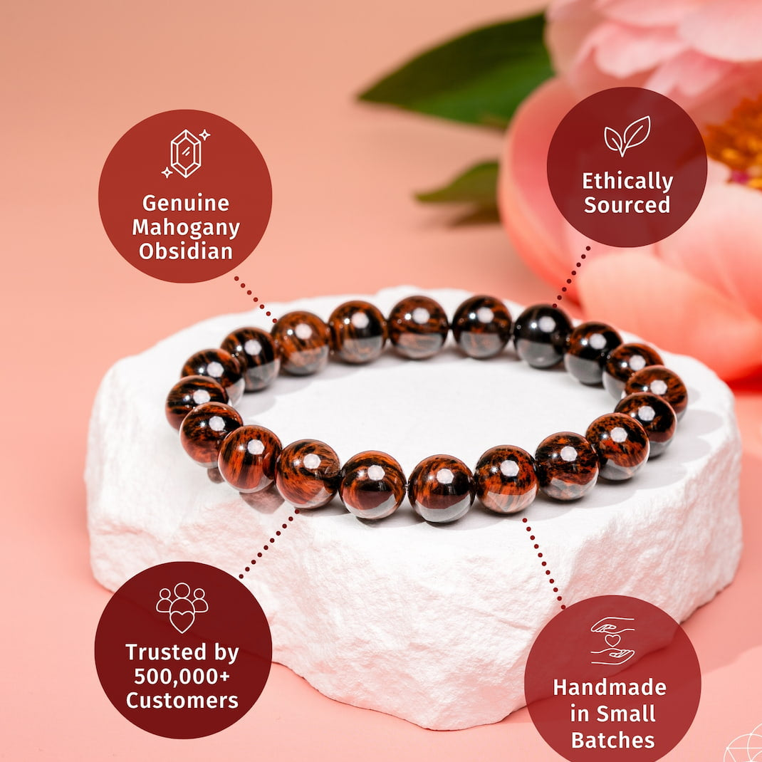 A beaded bracelet made of polished dark brown and black obsidian beads, displayed on a white stone pedestal against a soft pink background with decorative flowers. Four circular callout badges highlight product features: 'Genuine Mahogany Obsidian,' 'Ethically Sourced,' 'Trusted by 500,000+ Customers,' and 'Handmade in Small Batches.