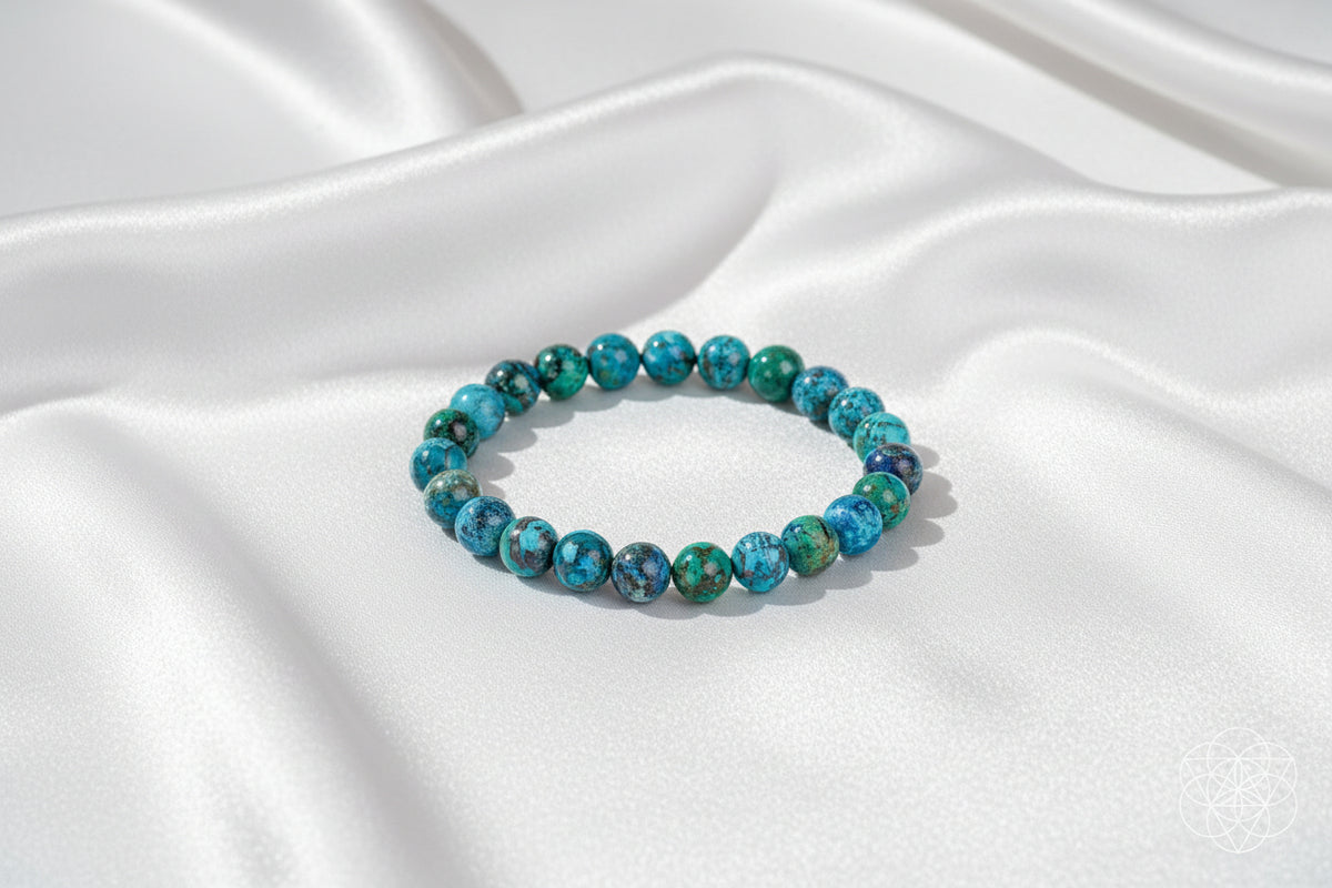 A beaded stretch bracelet made of marbled blue and green round beads, styled on a white silky background.