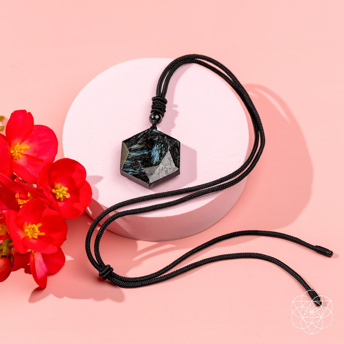 Black cord necklace with a geometric pendant on a pink background with red flowers