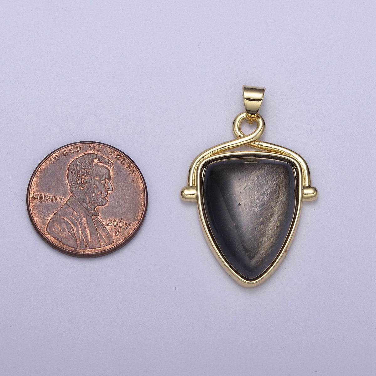 Gold pendant with a black stone next to a penny on a light purple background