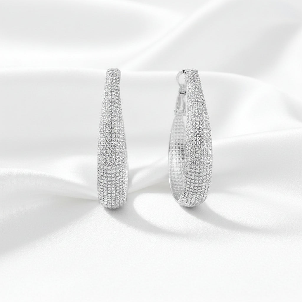 A pair of large silver hoop earrings with a textured, woven-like band design, shown on a white silky background.