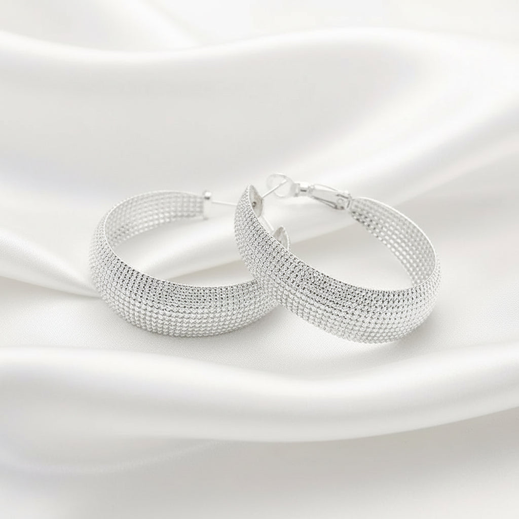 Sterling silver hoop earrings with a textured, diamond-like mesh pattern, displayed on white silky background