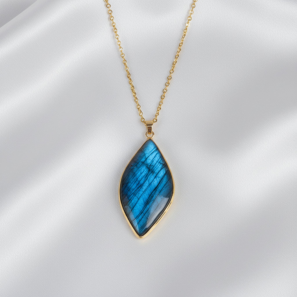A gold chain necklace with a teardrop-shaped blue labradorite pendant resting on a silk white surface.
