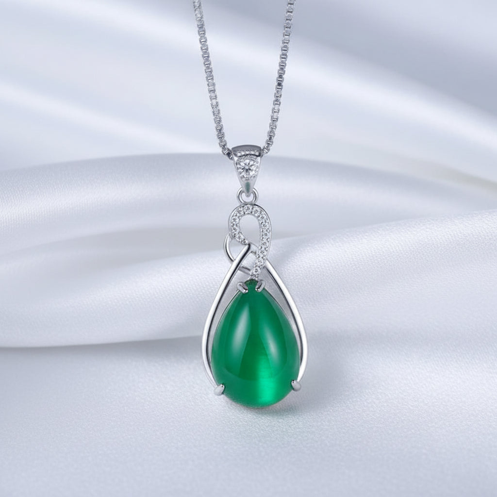 Green teardrop pendant with silver chain on a white textured surface