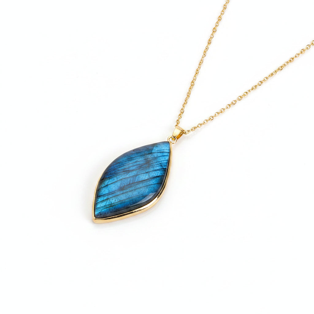 A gold chain necklace with a teardrop-shaped blue labradorite pendant resting on a white surface.