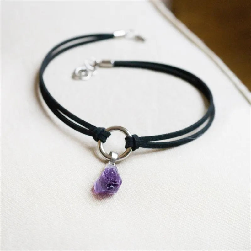 Black cord necklace with a purple crystal pendant on a white surface