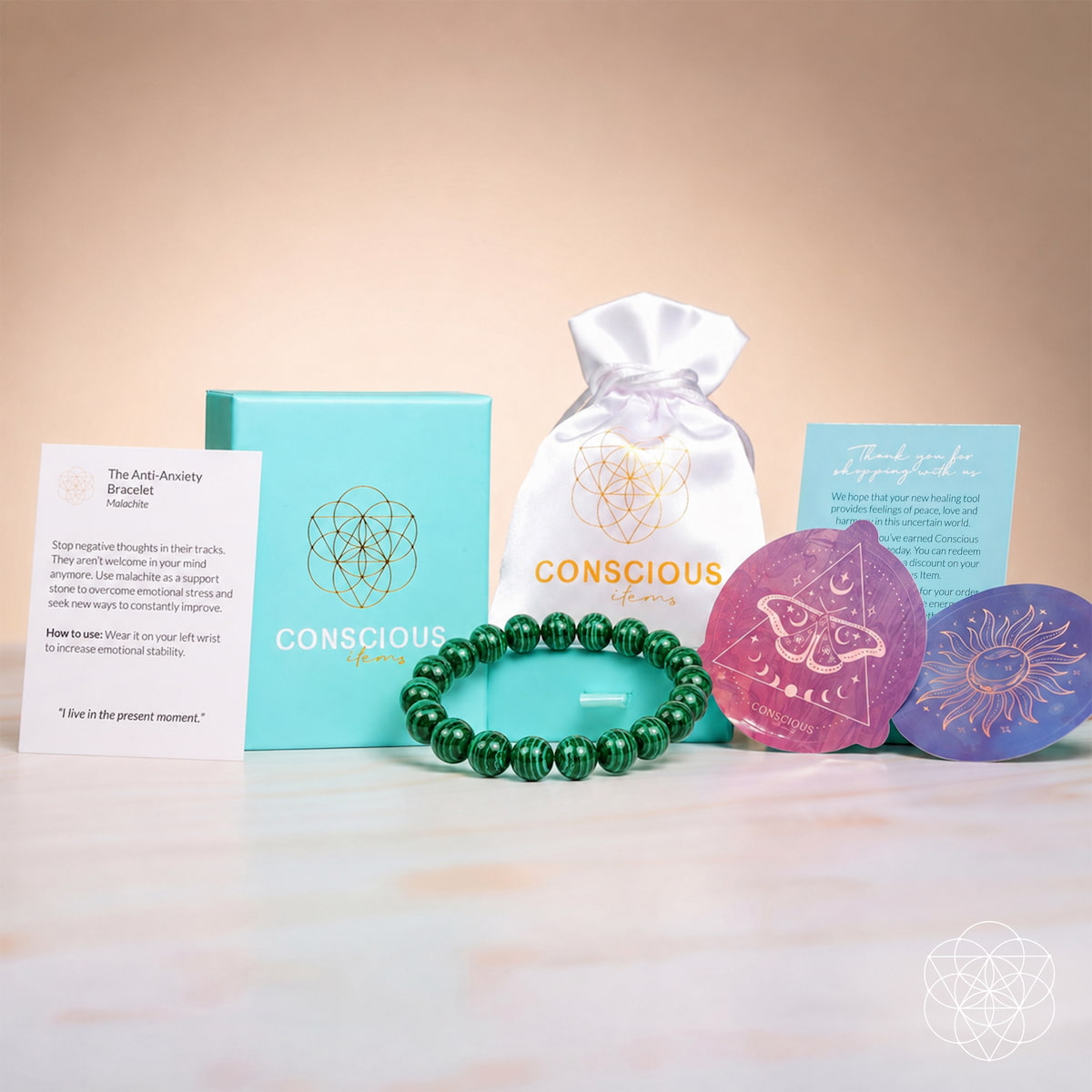 A Conscious brand gift set arranged on a light marble surface against a warm beige background. The set includes a turquoise box, a white drawstring pouch with the Conscious logo, a green beaded bracelet, two colorful circular cards or magnets, and two printed cards.