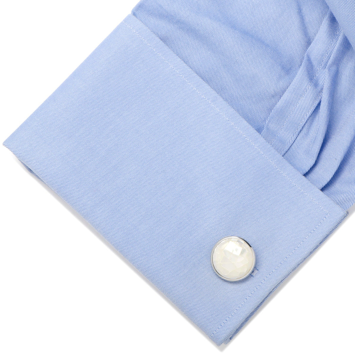 Close-up of a light blue shirt cuff with a pearl button on a white background