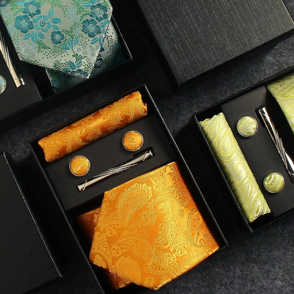 Collection of patterned fabric rolls and accessories in a black box on a dark surface.