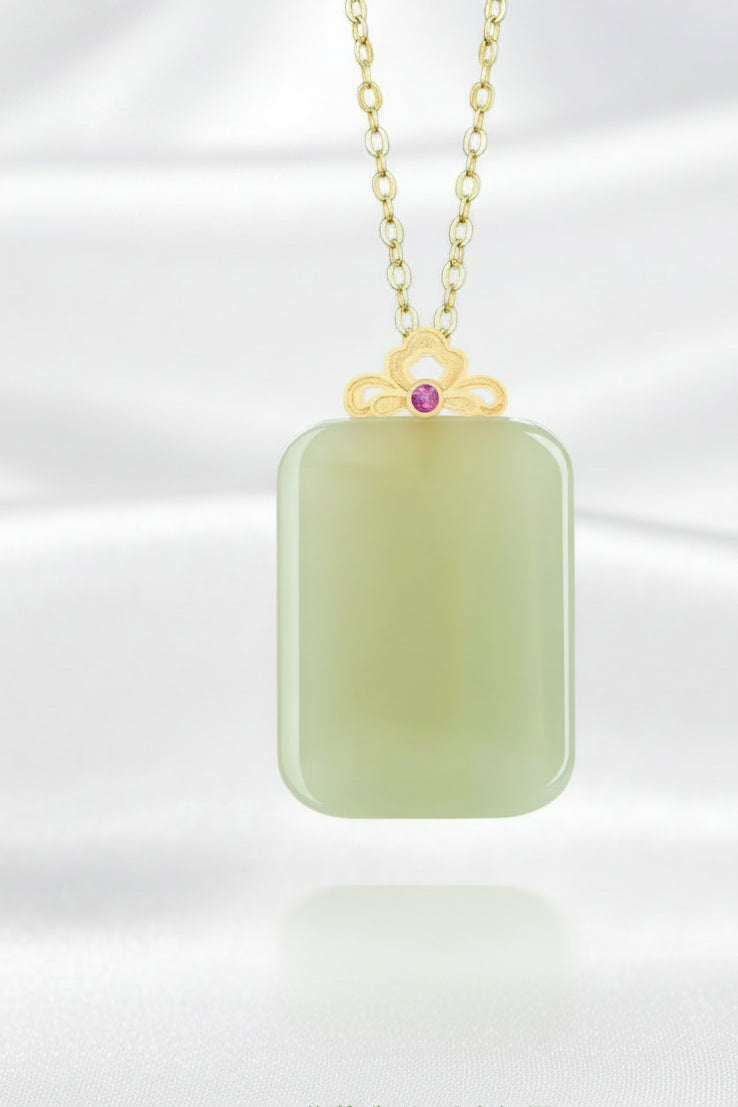 A Meng Fancy brand necklace featuring a natural green jade pendant with a gold-colored top loop and a small pink gemstone accent, set against a soft green background with Chinese text below.