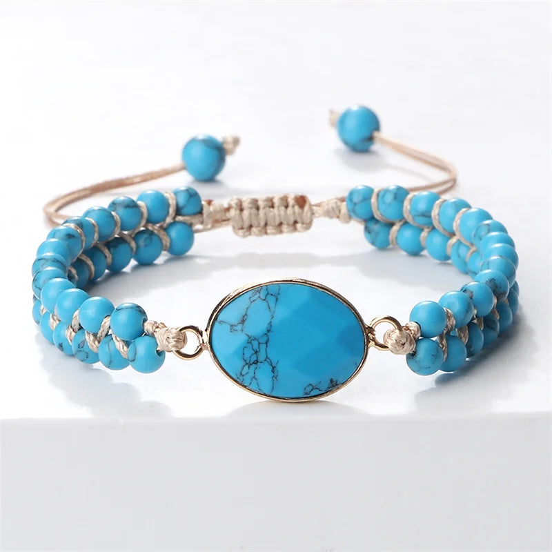 A turquoise beaded bracelet with a large oval turquoise centerpiece and gold-toned metal accents, displayed on a clean white surface.