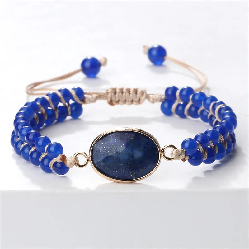 A beaded stretch bracelet featuring a central oval dark blue stone with gold glitter, surrounded by small blue beads and wrapped in gold-toned cord, shown on a white background.