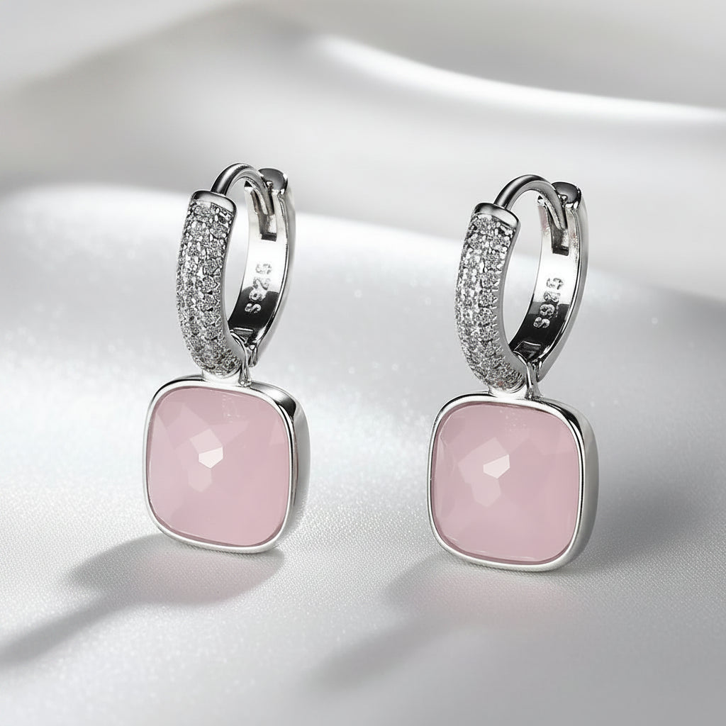 A pair of MEEKCAT silver huggie hoop earrings with square pink faceted gemstones and pavé-set clear crystals, displayed on a white surface with a dark background.