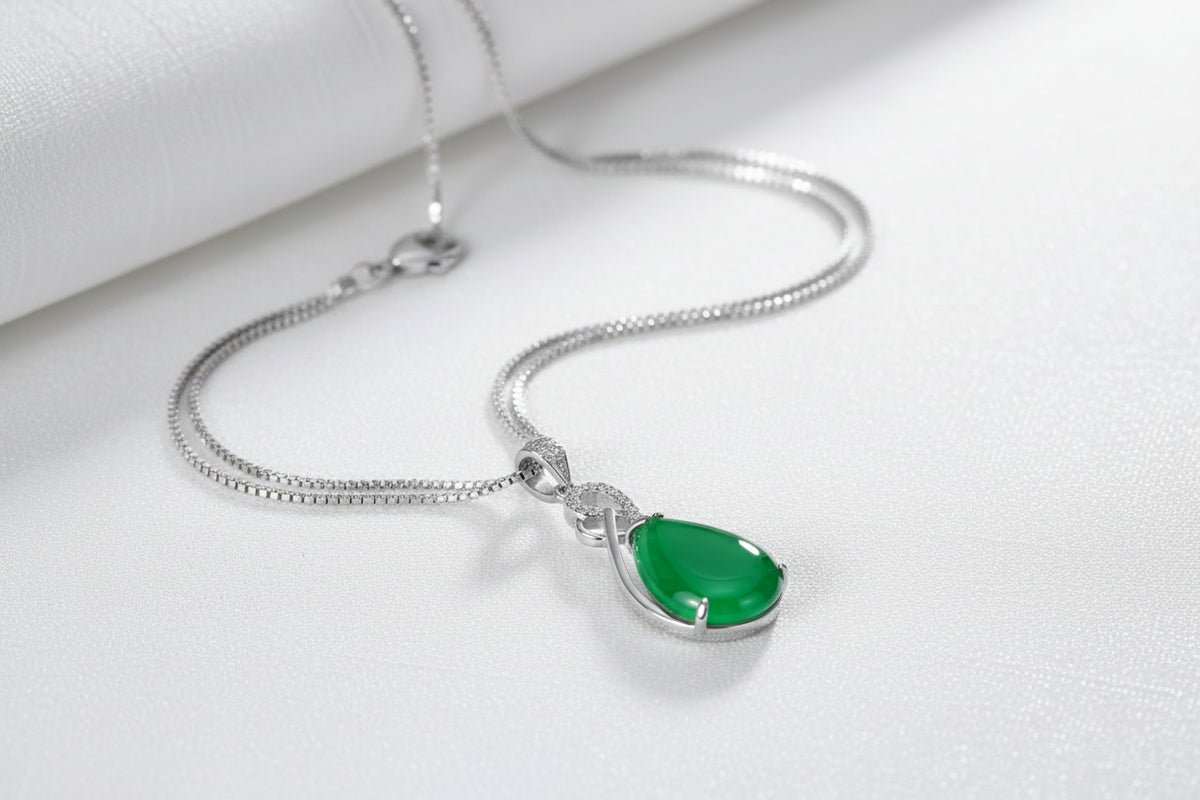 Green teardrop pendant necklace on a white textured surface