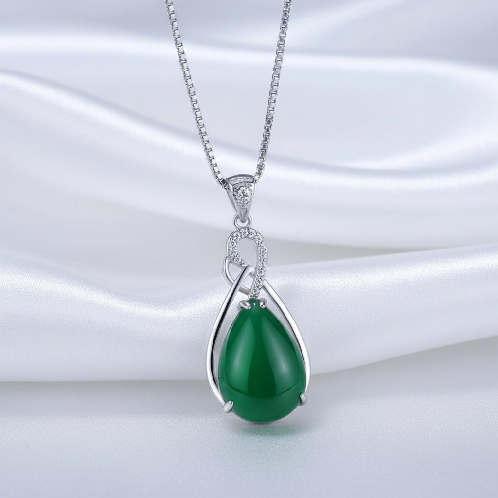 Green teardrop pendant with silver chain on a white textured surface
