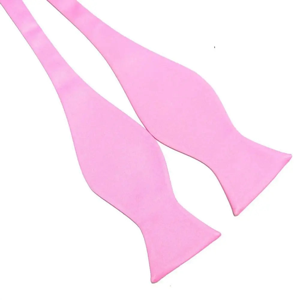 A pair of light pink pre-tied bow ties arranged diagonally on a plain white background.