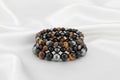 Stack of beaded bracelets with black, orange, and gray beads on a white background