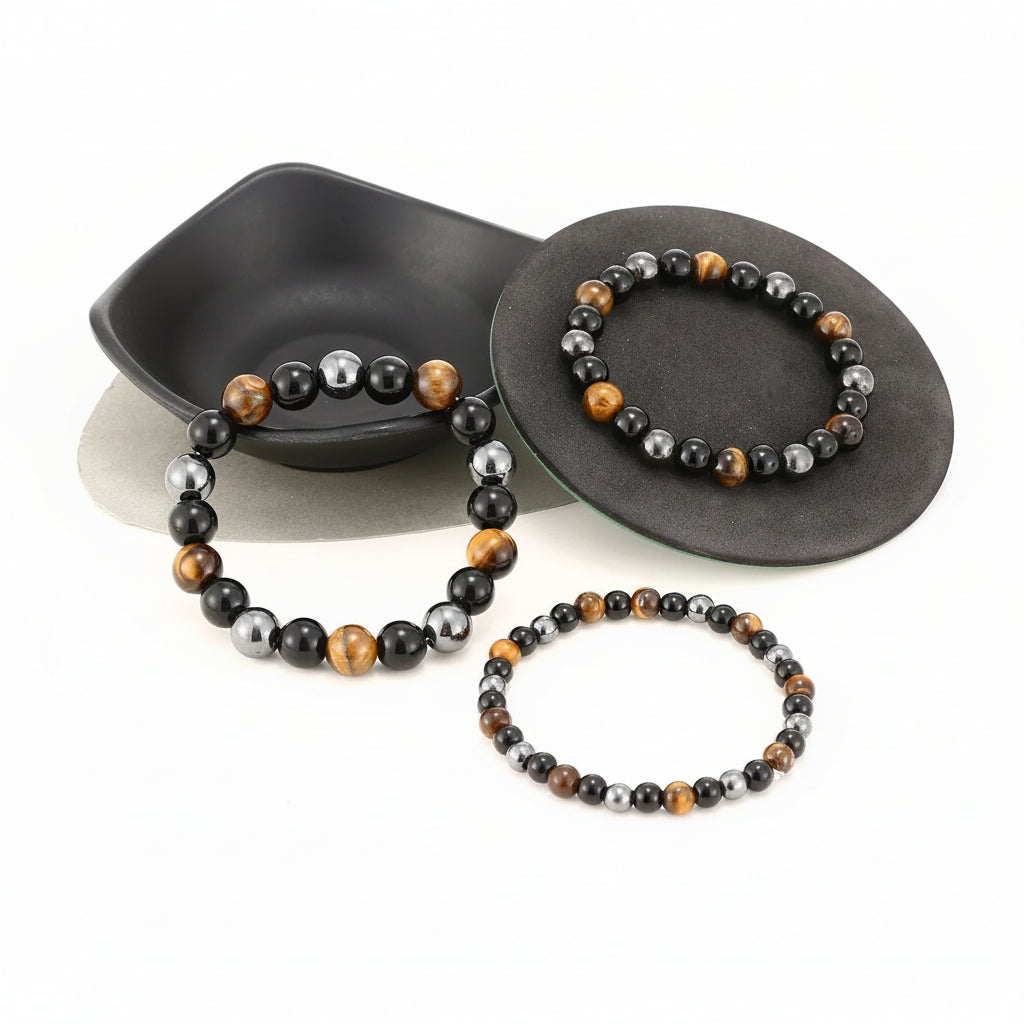 Three beaded stretch bracelets displayed on black oval jewelry stands against a white background. The bracelets feature alternating beads of black, metallic silver, brown, and tiger's eye.