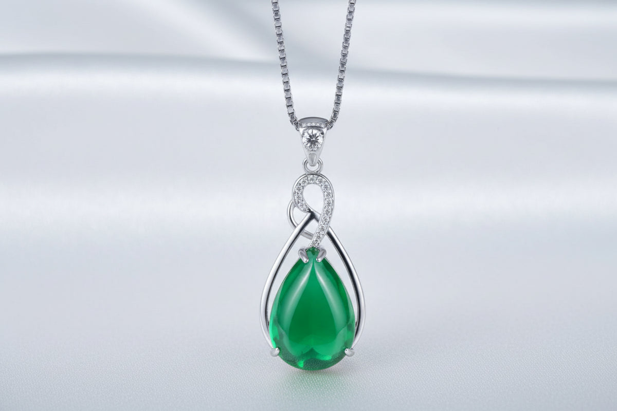 Green teardrop pendant with silver chain on a white textured surface