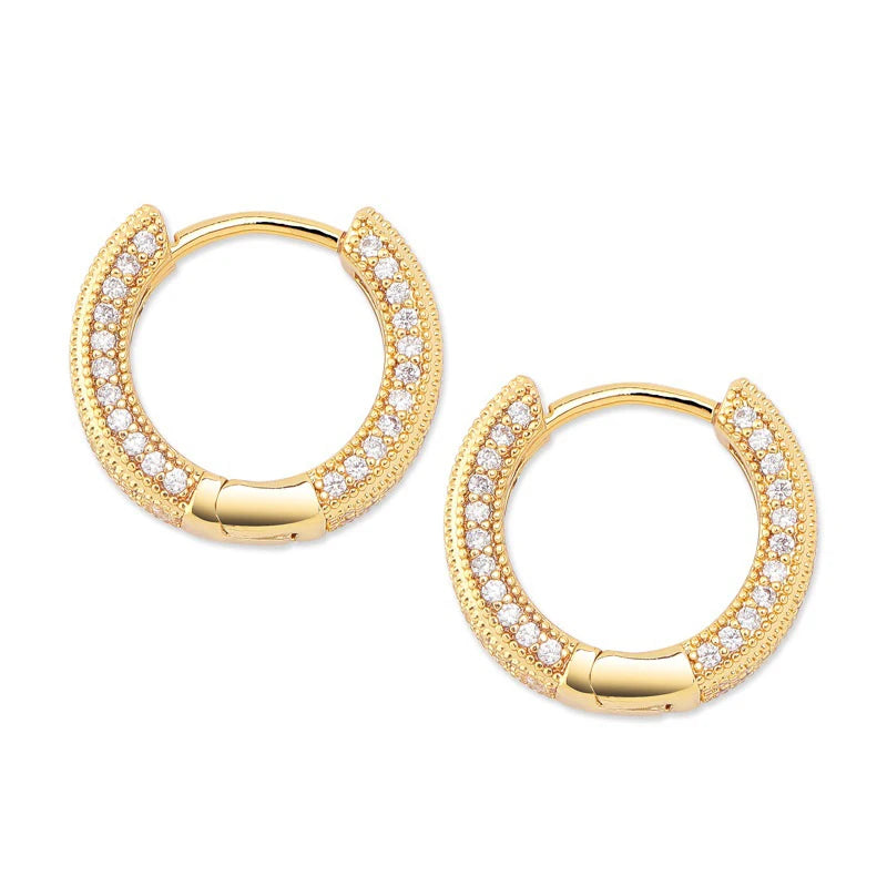 A pair of gold huggie hoop earrings adorned with pavé-set clear stones and a polished clasp, shown on a solid white background.