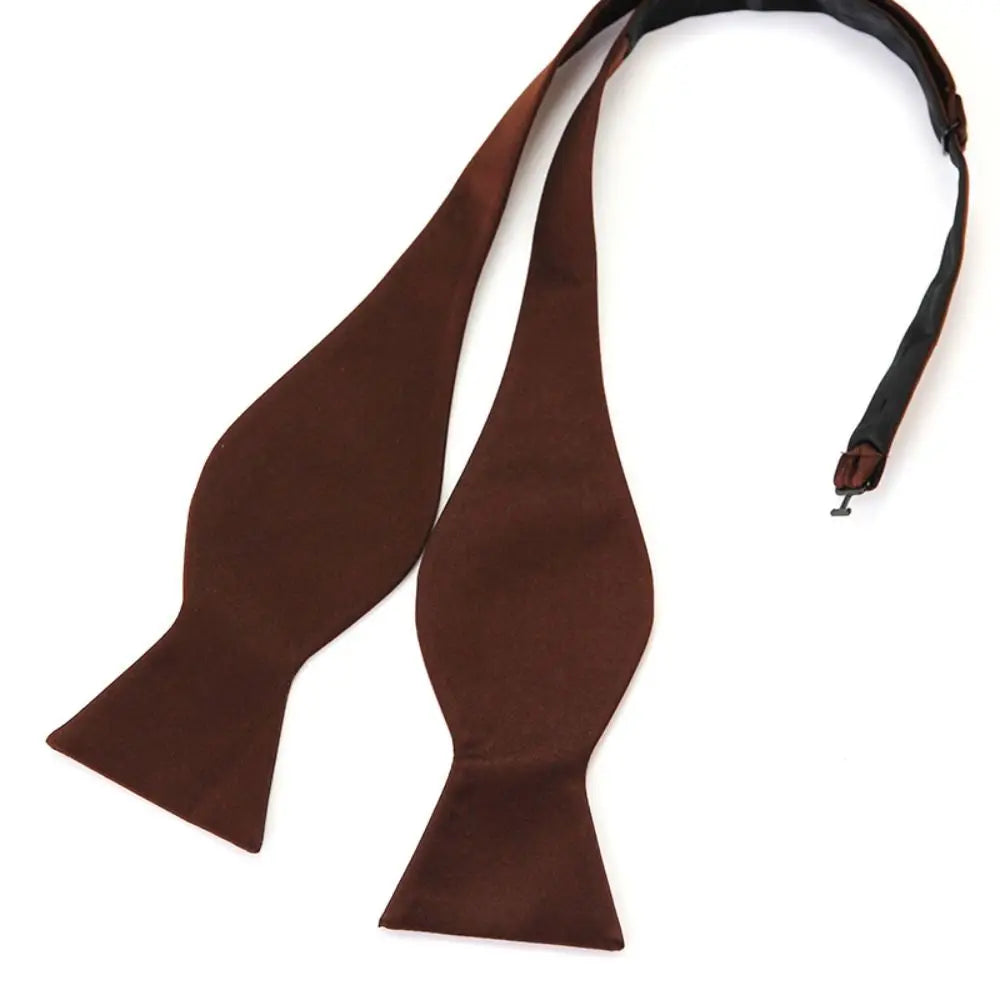 A pre-tied brown bow tie made of smooth fabric, displayed on a clean white background with its black adjustable neck strap visible.