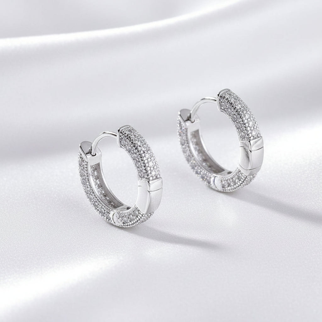 A pair of silver-toned huggie hoop earrings adorned with small clear stones