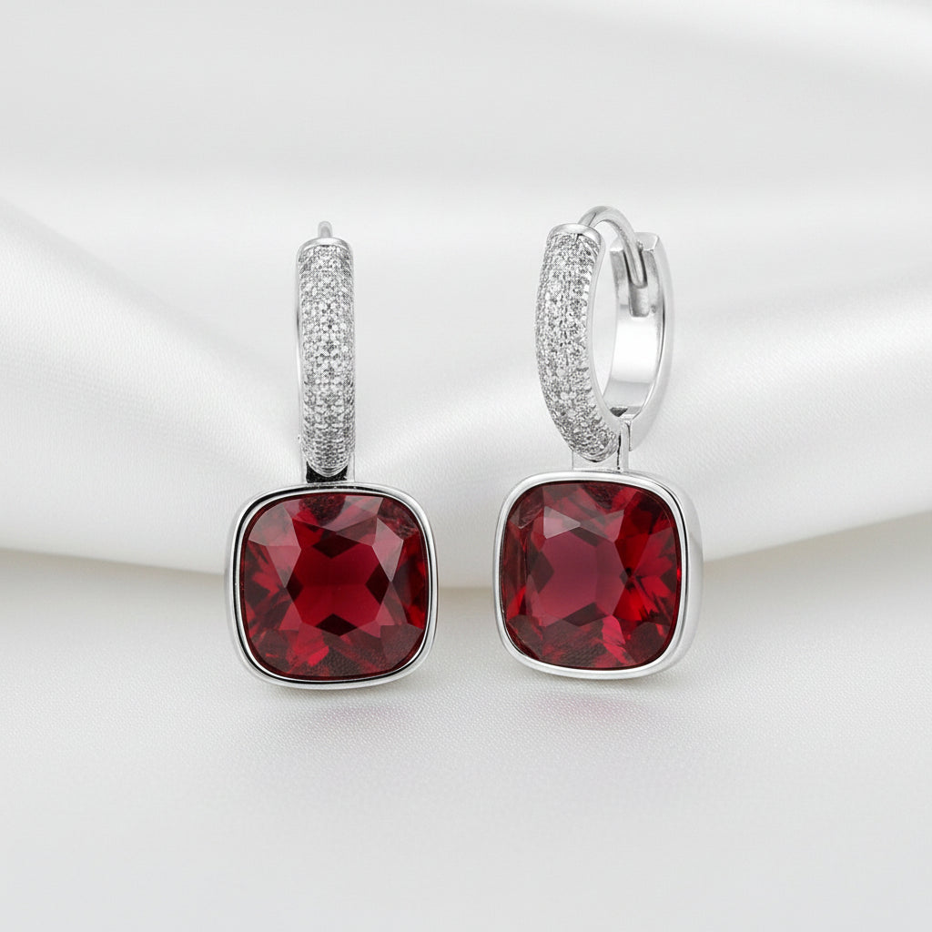 A pair of MEEKCAT sterling silver huggie hoop earrings with large square-cut red gemstones and a row of small clear stones in the hoops. The image includes dimension markings of 11mm width and 25mm height, a 'REAL STERLING 925' seal, and the MEEKCAT brand name on a white background.