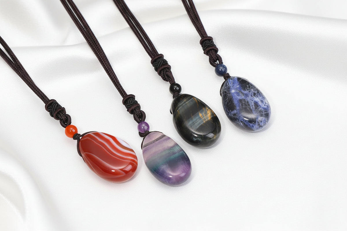 Three stone pendants on black cords with silky white background