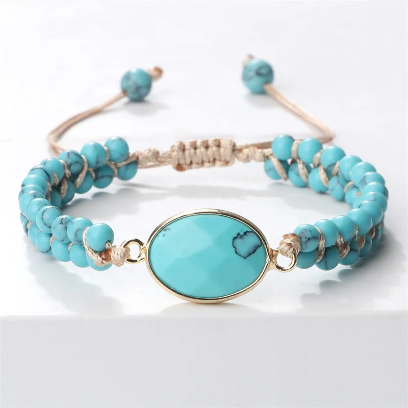 A turquoise beaded bracelet with a large oval turquoise stone centerpiece in a gold-tone frame, wrapped with tan cord, on a white background.