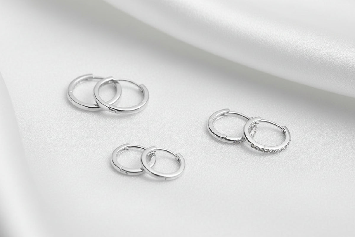 Four pairs of silver hoop earrings arranged on a textured black surface with a white silky background.