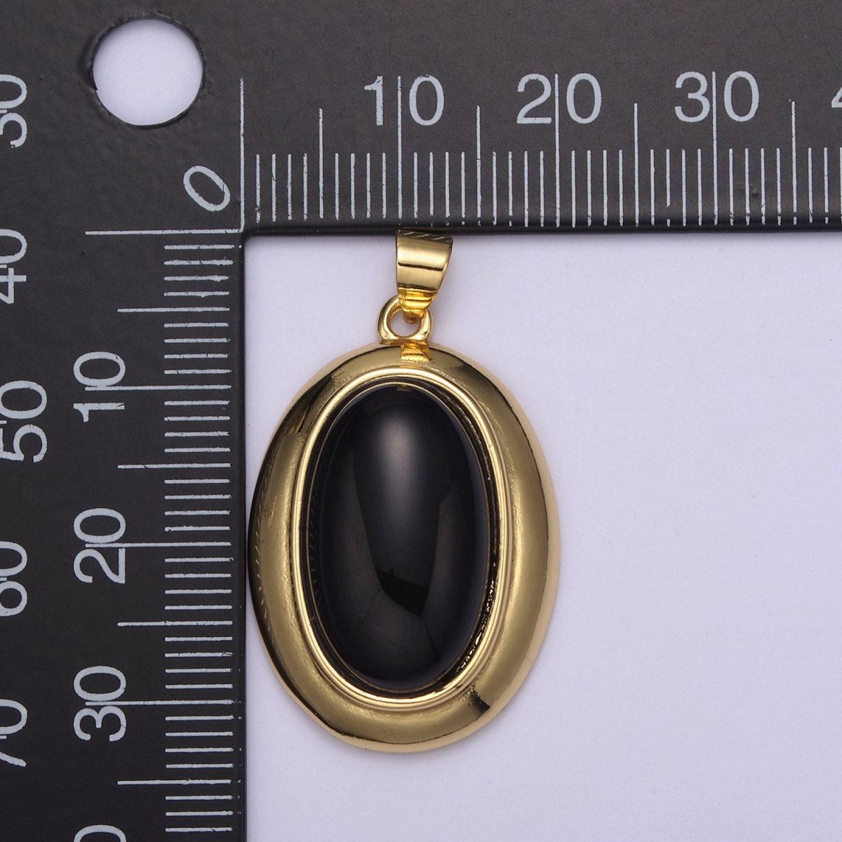 Gold pendant with a black stone on a white background with a ruler for scale.