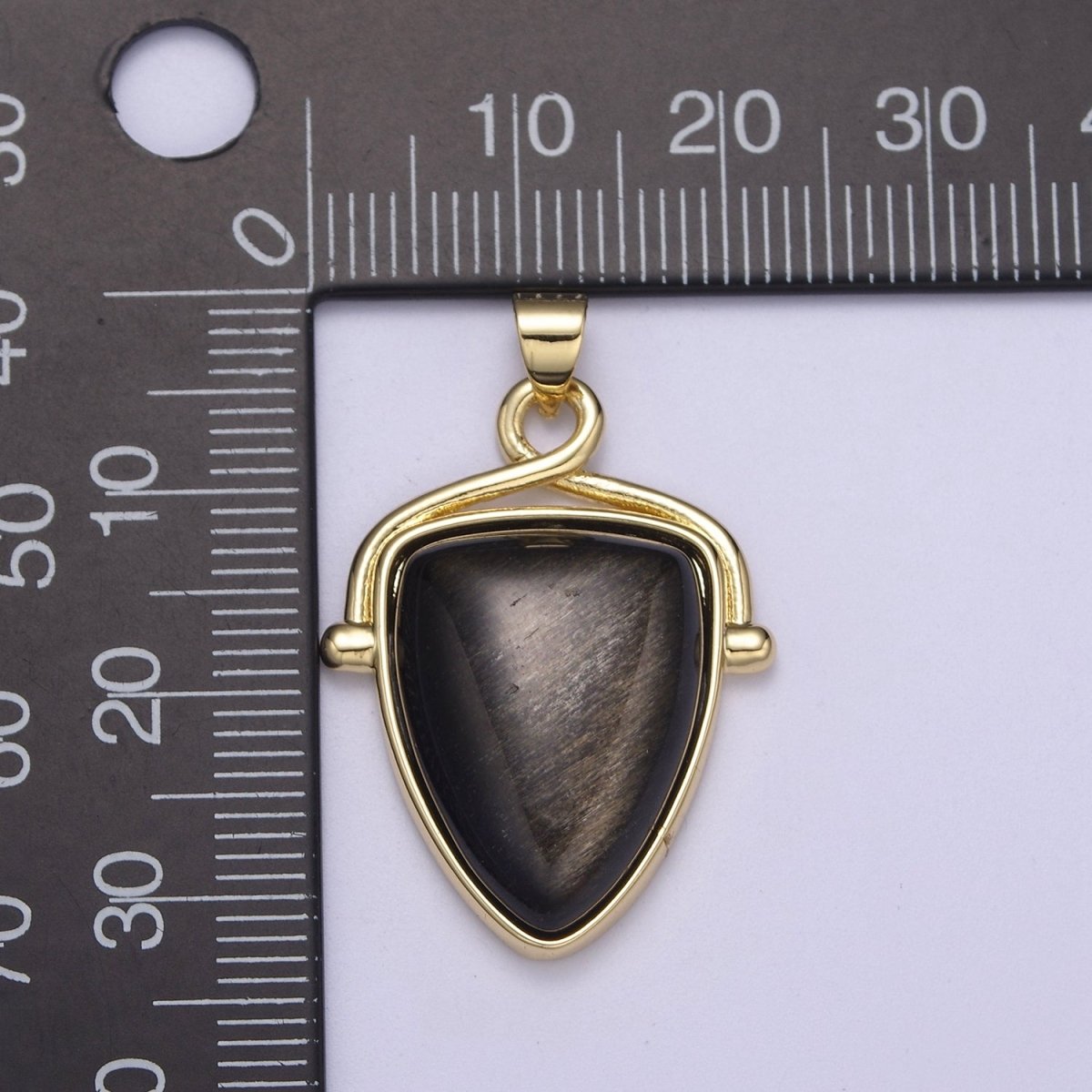 Gold pendant with a dark stone against a ruler for scale