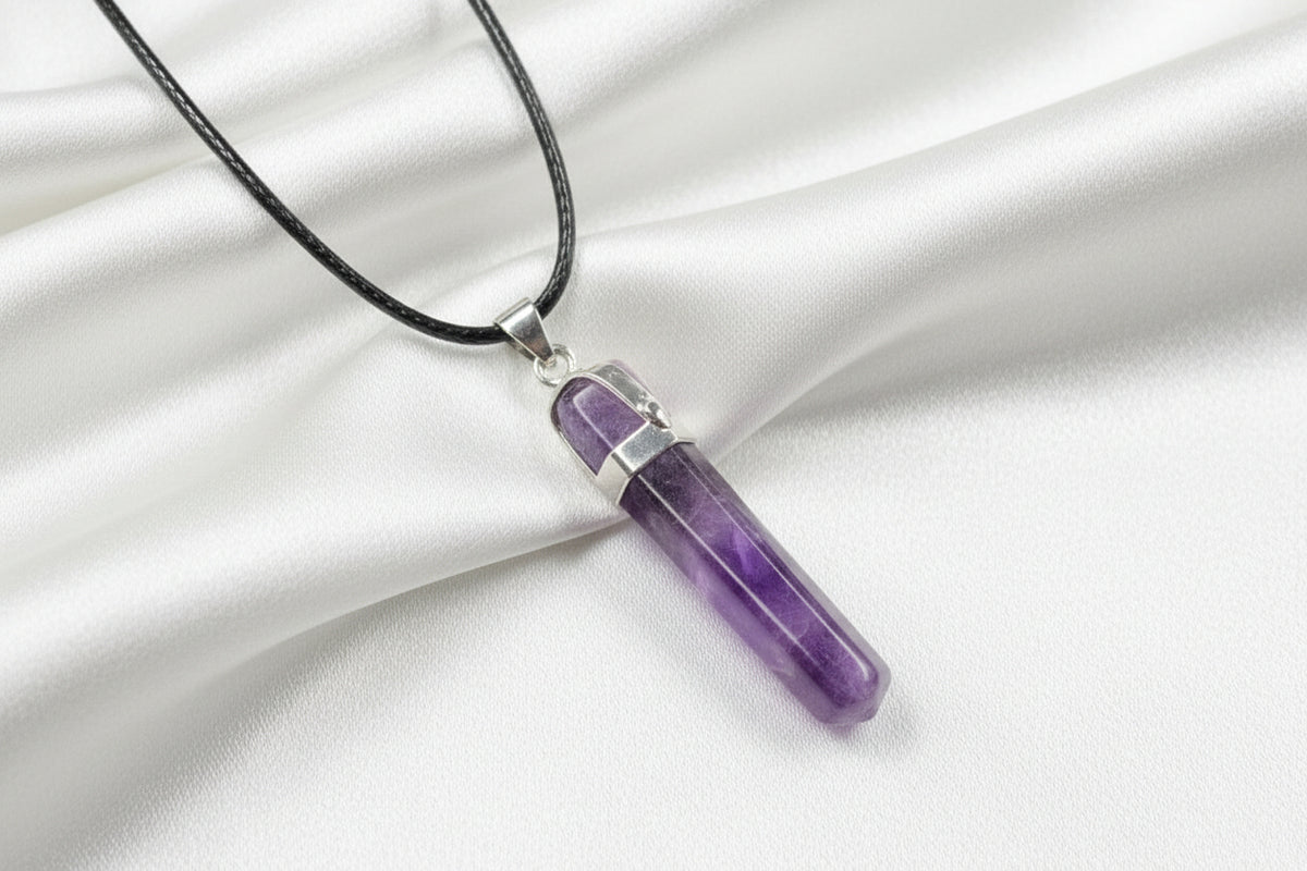 A purple amethyst cylindrical pendant necklace with a silver-toned metal cap and a black cord, shown on a textured dark gray background.