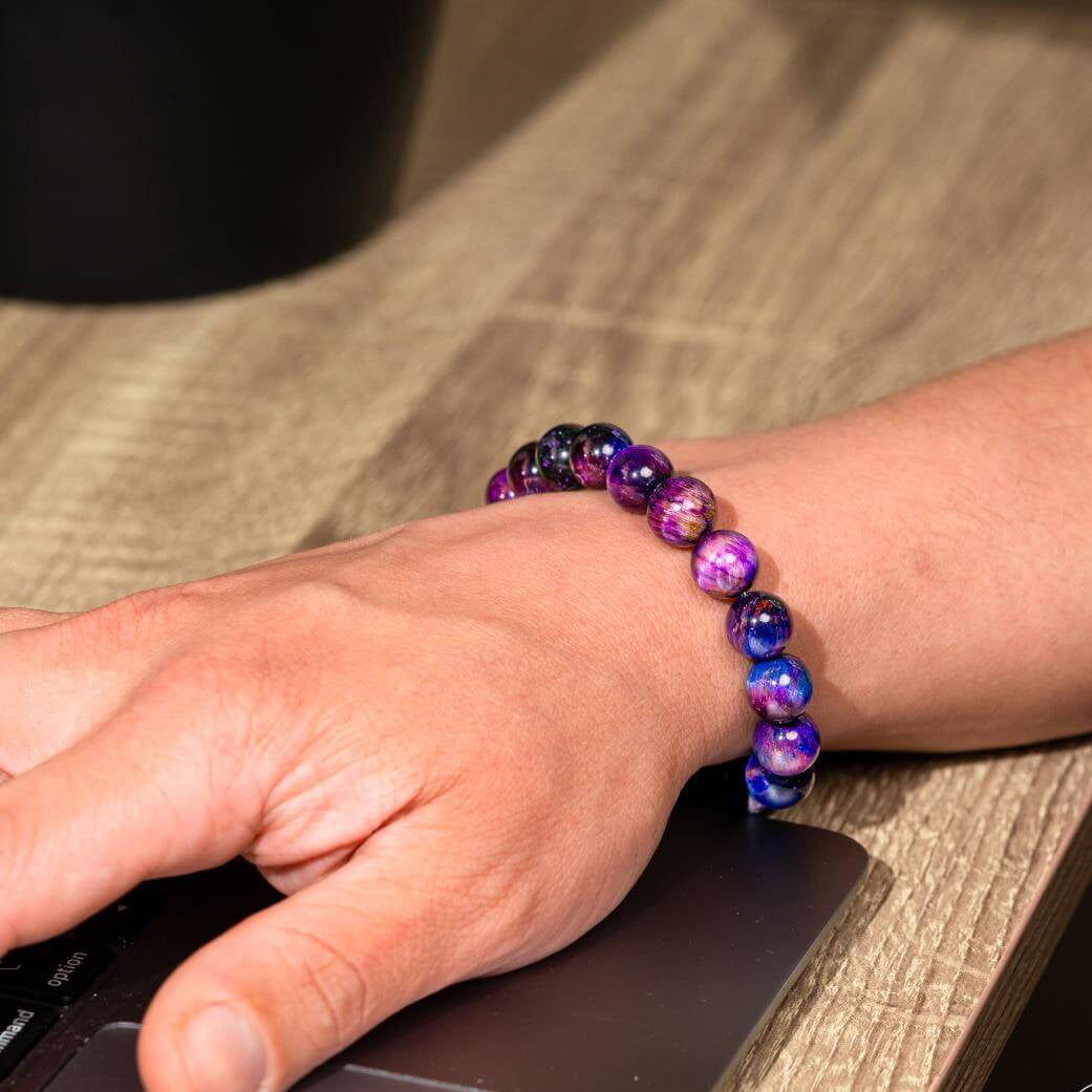 Person using a computer mouse with a colorful beaded bracelet on a wooden surface
