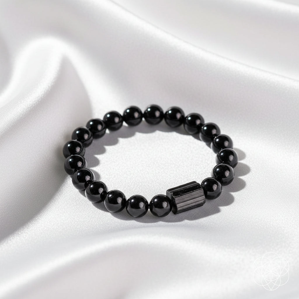 A black beaded bracelet with a polished rectangular black stone accent, displayed on a white silky background.