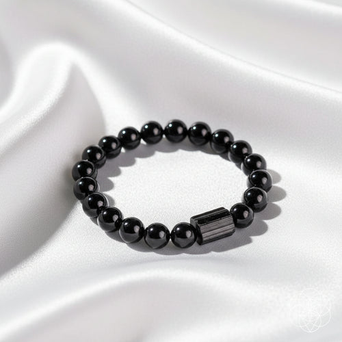 A black beaded bracelet with a polished rectangular black stone accent, displayed on a white silky background.