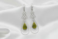 A pair of silver dangle earrings with teardrop-shaped olive green gemstone pendants, shown against a plain white background.