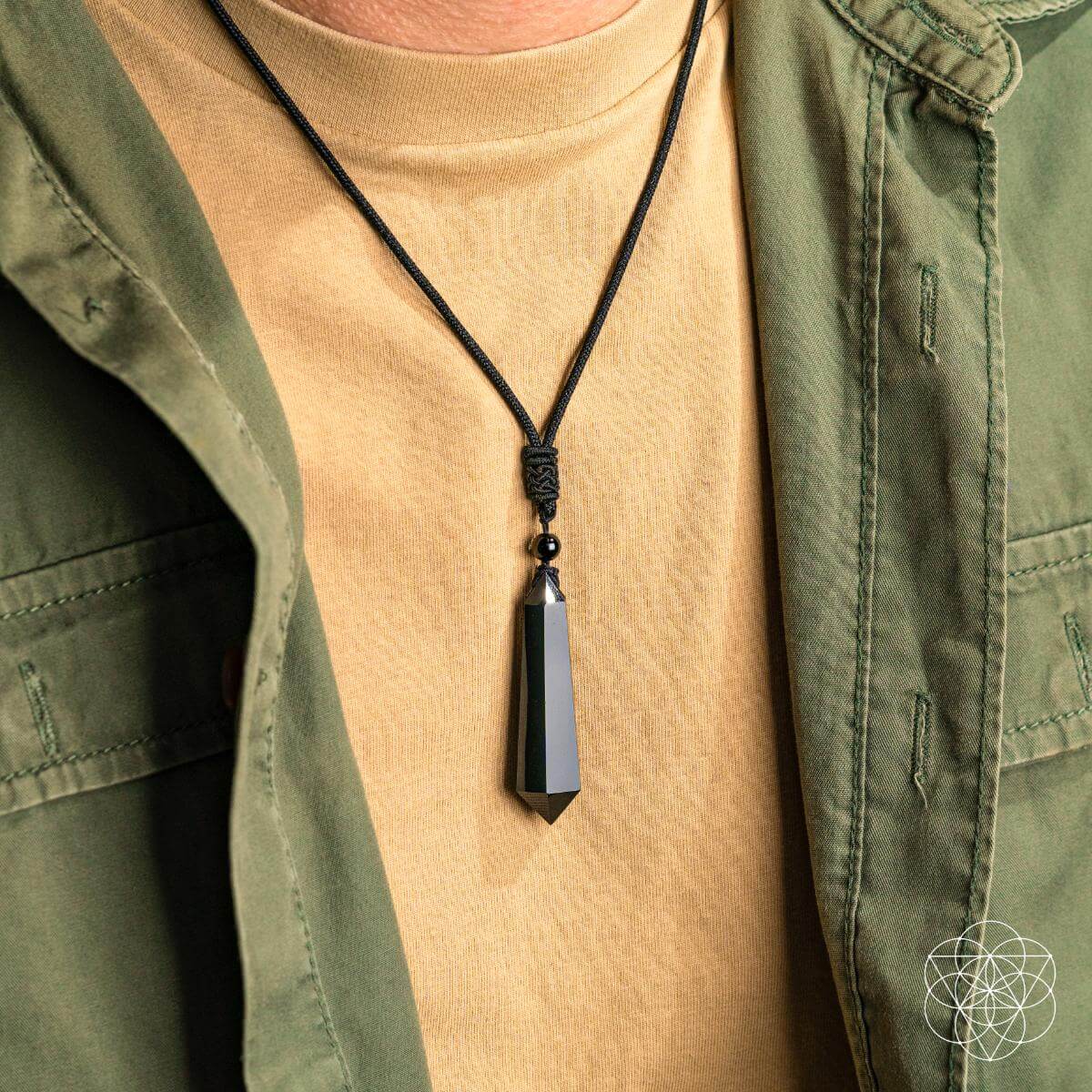 Person wearing a green jacket over a beige shirt with a black pendant necklace.