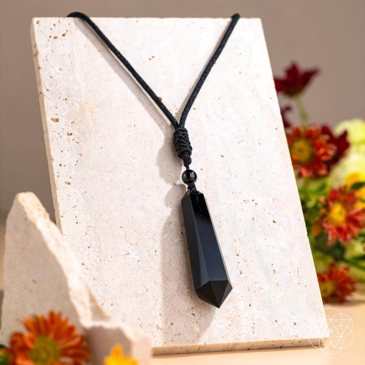 Black pendant necklace on a white stand with flowers in the background