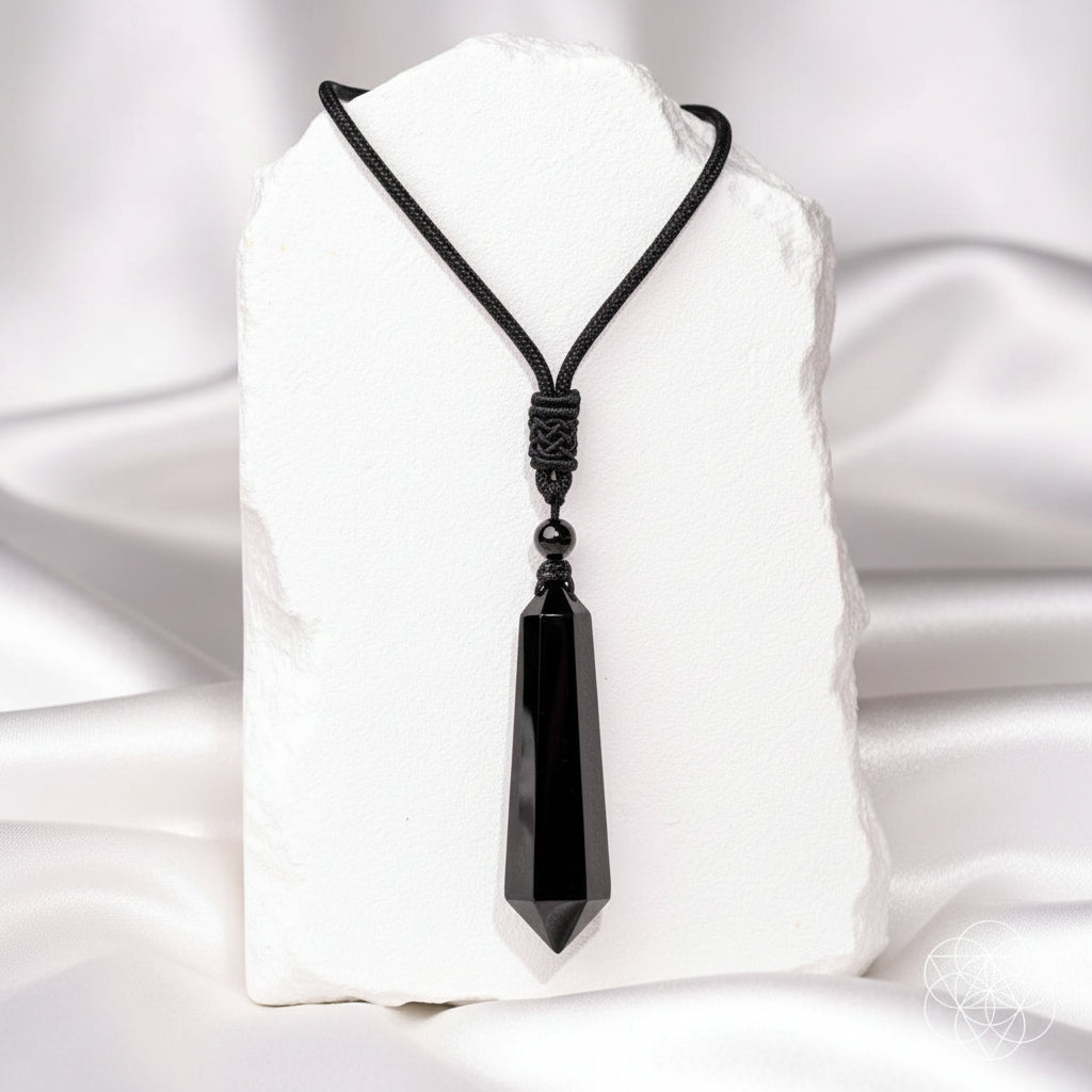 A black crystal point pendant necklace displayed on a white stone block against a white silky background.
