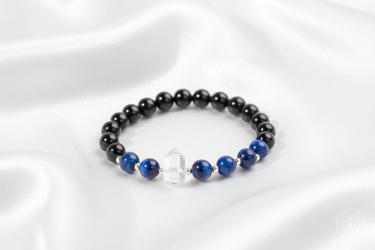 A beaded bracelet with glossy black round beads, deep blue lapis lazuli-style beads, a clear faceted crystal charm, and silver spacer beads, arranged on a white silky background.